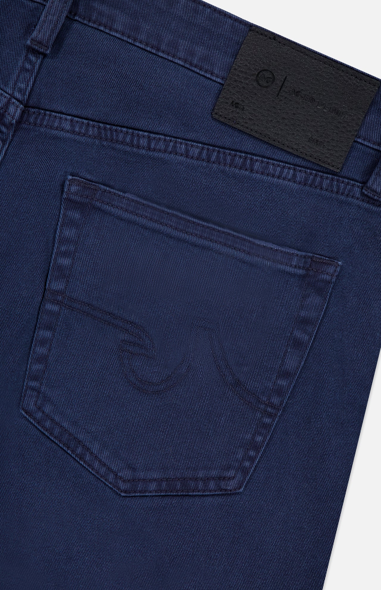 Close-up of the back pocket on AG Everett Slim Stretch Jeans in navy, showcasing a subtle stitched pocket design and a black leather AG brand patch on the waistband.