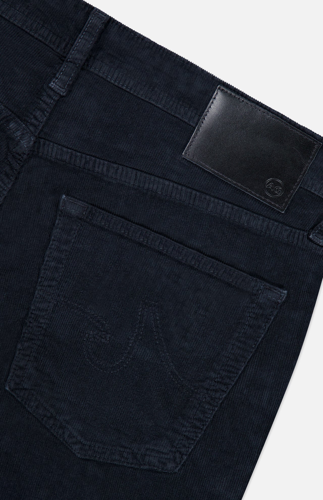 Close-up of the back pocket and waistband of the AG Everett Slim Corduroy Pant in dark blue, featuring a black leather brand patch and tonal stitching, highlighting its modern slim fit silhouette.