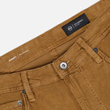 Close-up of the waistband and front pockets of the AG Everett Corduroy Pant in Bronze, featuring a slim fit, metal button, zipper, belt loops, and brand labels on the inside waistband, all set against a white background.