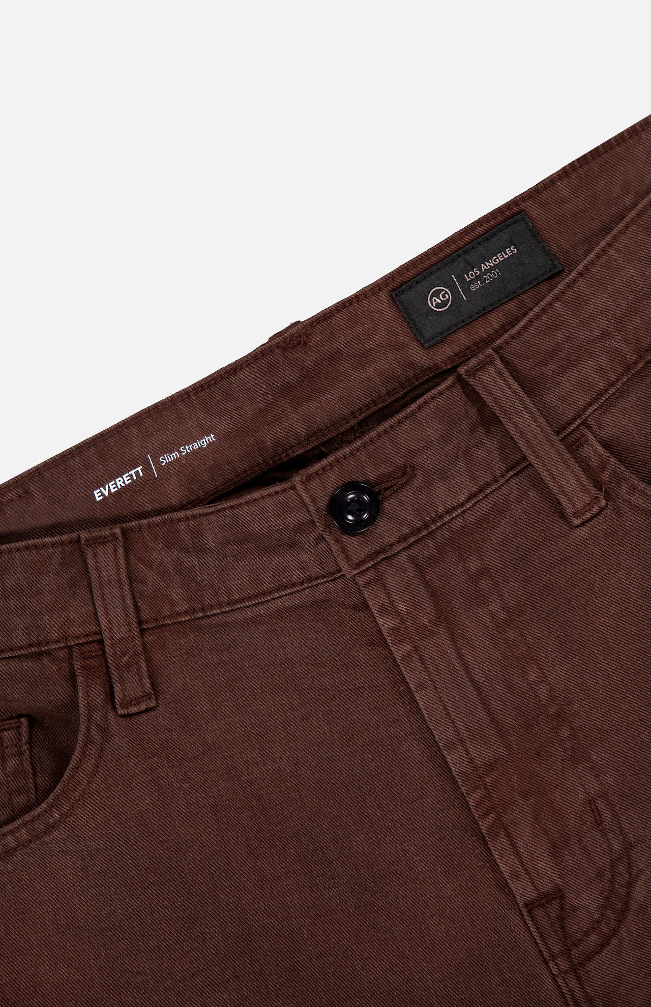 Close-up of the waistband and front pockets of AG's Everett Pants in Sulfur, showcasing a black button, belt loops, and an inner label with text including “Everett,” “Slim Straight,” and slim fit details.