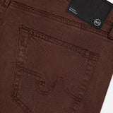 Close-up of the back pocket and waistband of AG's Everett Pants in Sulfur, slim fit brown denim with stitching details and a black rectangular AG brand label on the waistband.