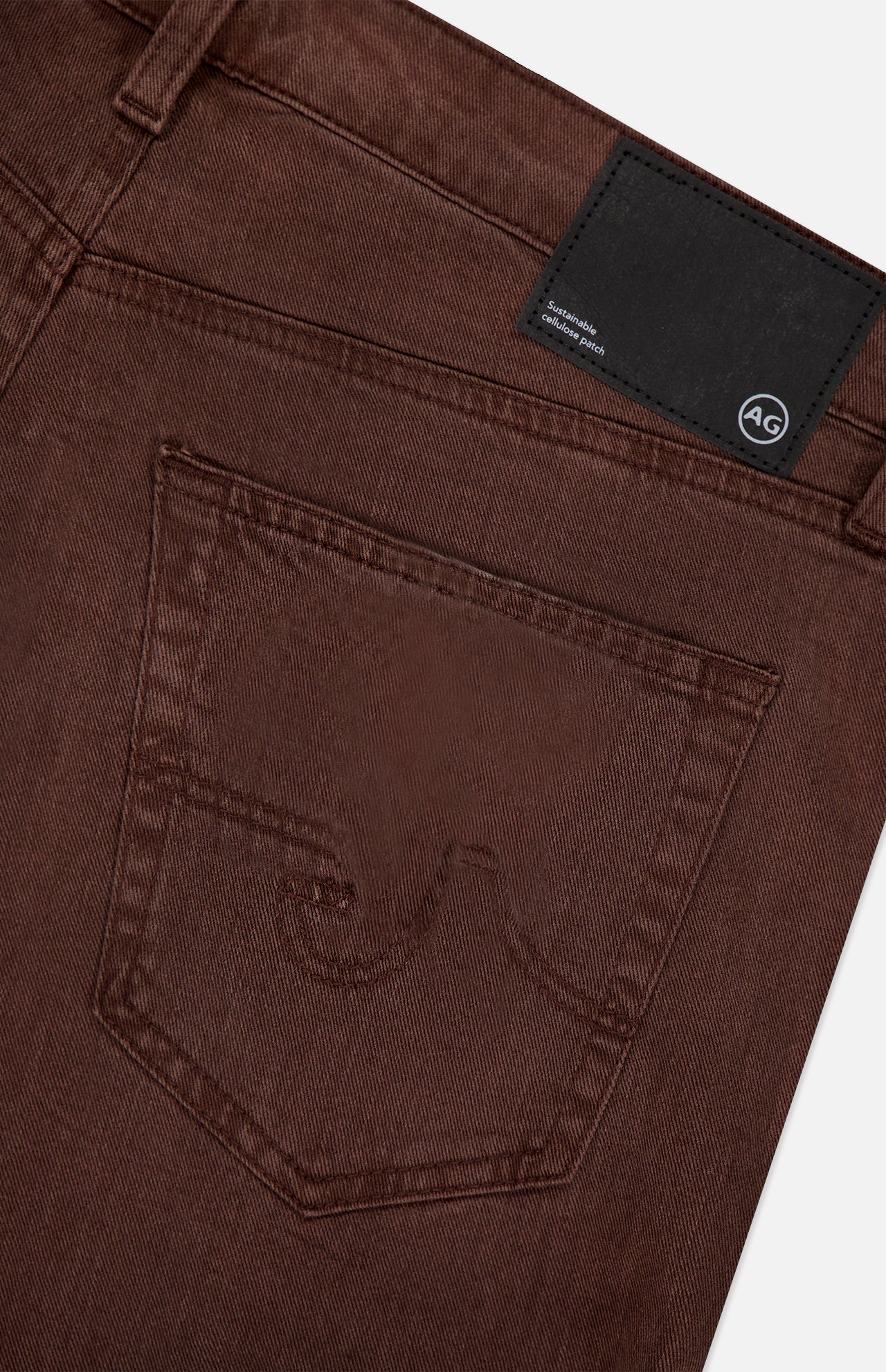 Close-up of the back pocket and waistband of AG's Everett Pants in Sulfur, slim fit brown denim with stitching details and a black rectangular AG brand label on the waistband.