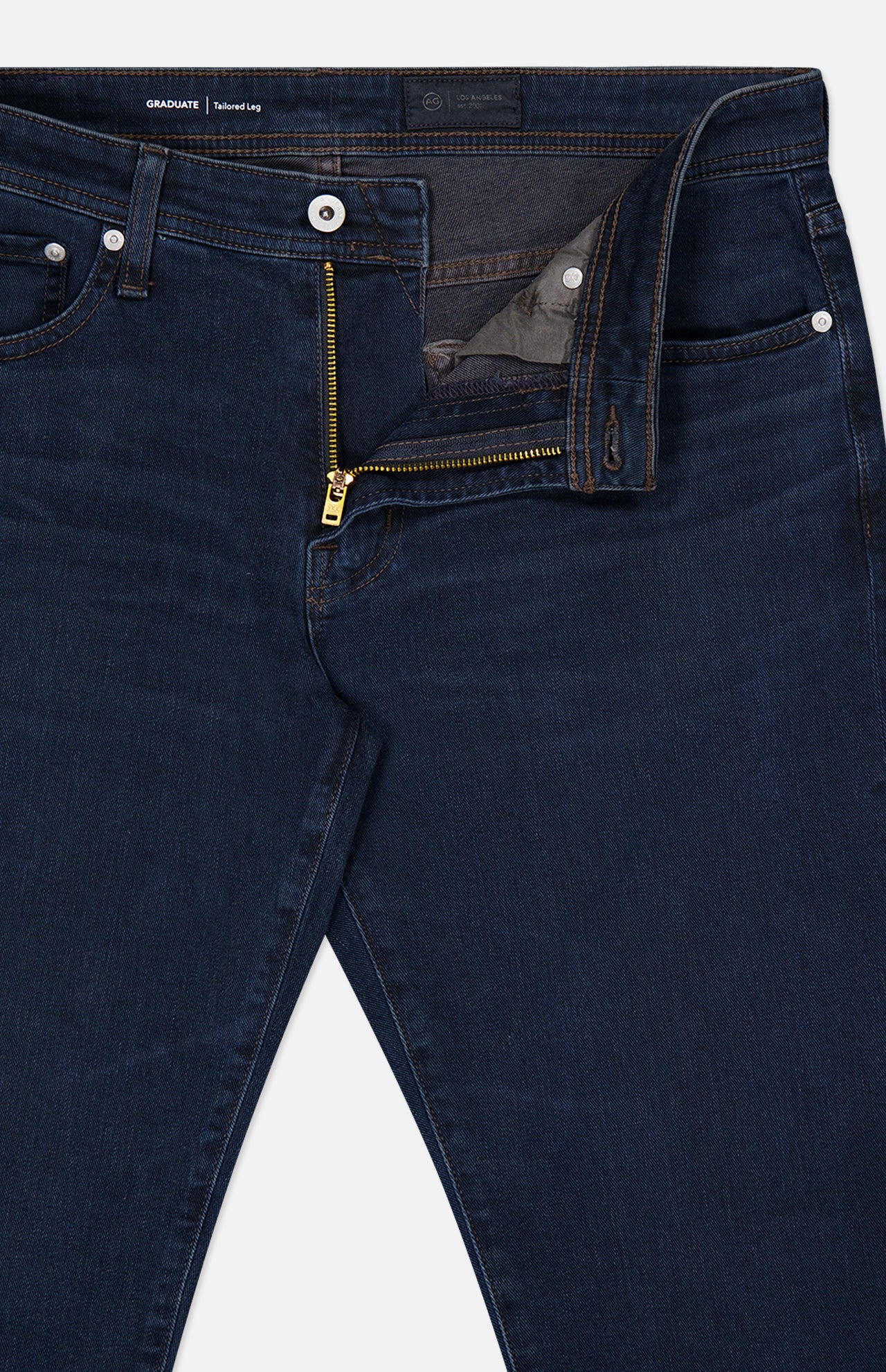 Graduate Pant in Studio by AG, showcasing an ultra-dark blue wash with vintage-inspired details, brass zipper, and white button fly—partially unzipped and unbuttoned to reveal the waistband and inner pocket lining—displayed against a plain background.
