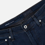 Close-up of the waistband and upper portion of the AG Graduate Pant in Studio, featuring a button closure, zipper fly, belt loops, and visible stitching on the pockets. The interior label reads GRADUATE | Tailored Leg, emphasizing vintage-inspired detailing throughout the design.