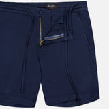 The Oliver Drawstring Shorts by AG, featuring a navy color, drawstring waist, elastic waistband, mid rise fit, side pockets, and partially unzipped front fly, are shown laid flat on a white background.