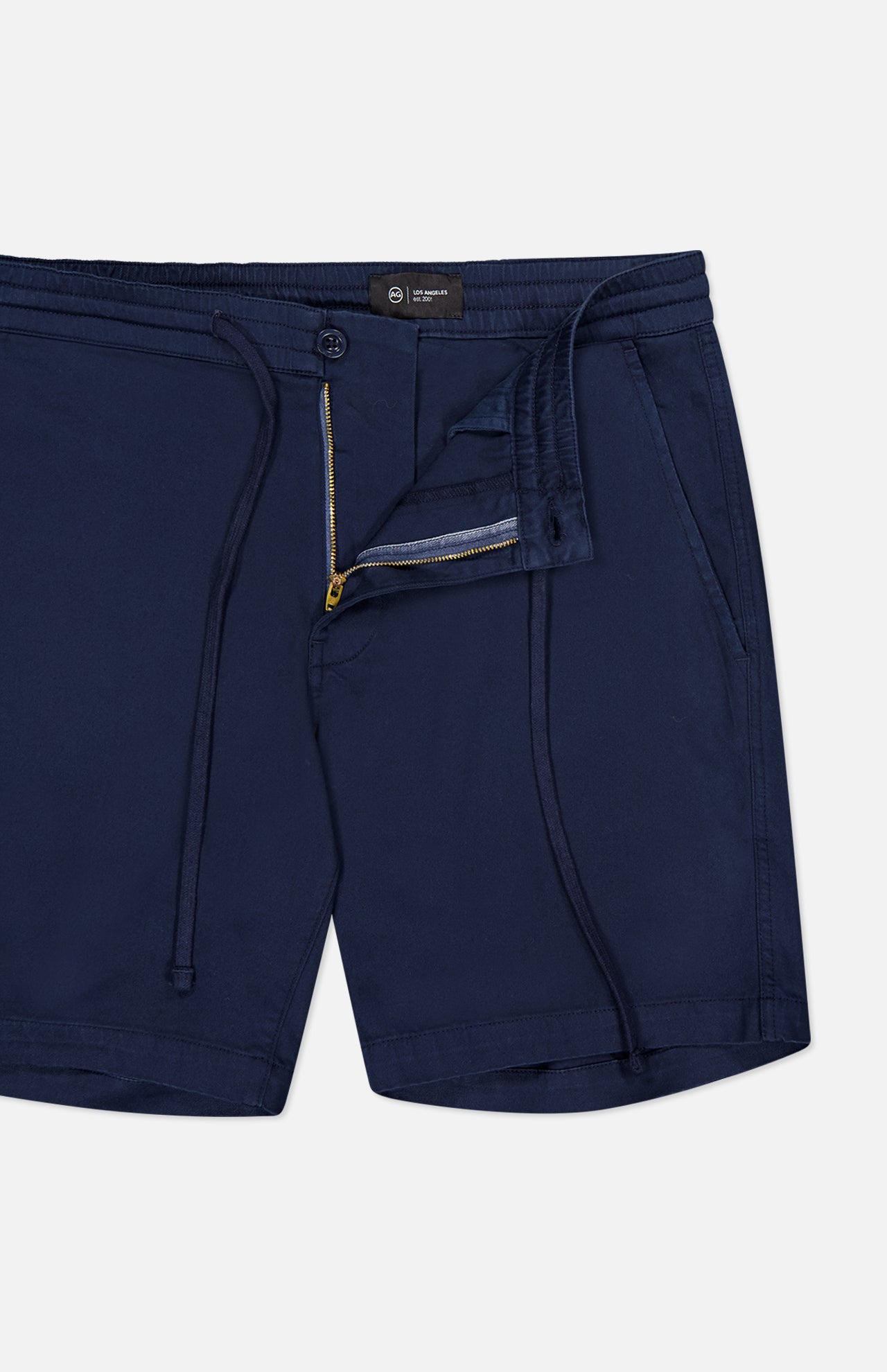 The Oliver Drawstring Shorts by AG, featuring a navy color, drawstring waist, elastic waistband, mid rise fit, side pockets, and partially unzipped front fly, are shown laid flat on a white background.