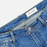 Close-up of the Protege Jean in 14 Years by AG, featuring blue denim with visible stitching, belt loops, a button closure, and a white label reading “AG AGED DENIM” inside the waistband. The straight leg fit is accentuated by subtle vintage details throughout the fabric.