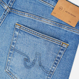 Close-up of blue denim jeans showing a back pocket with vintage detail stitching and a brown leather patch labeled AG near the waistband. The Protege Jean in 14 Years by AG features a straight leg fit, highlighting classic craftsmanship and timeless appeal.