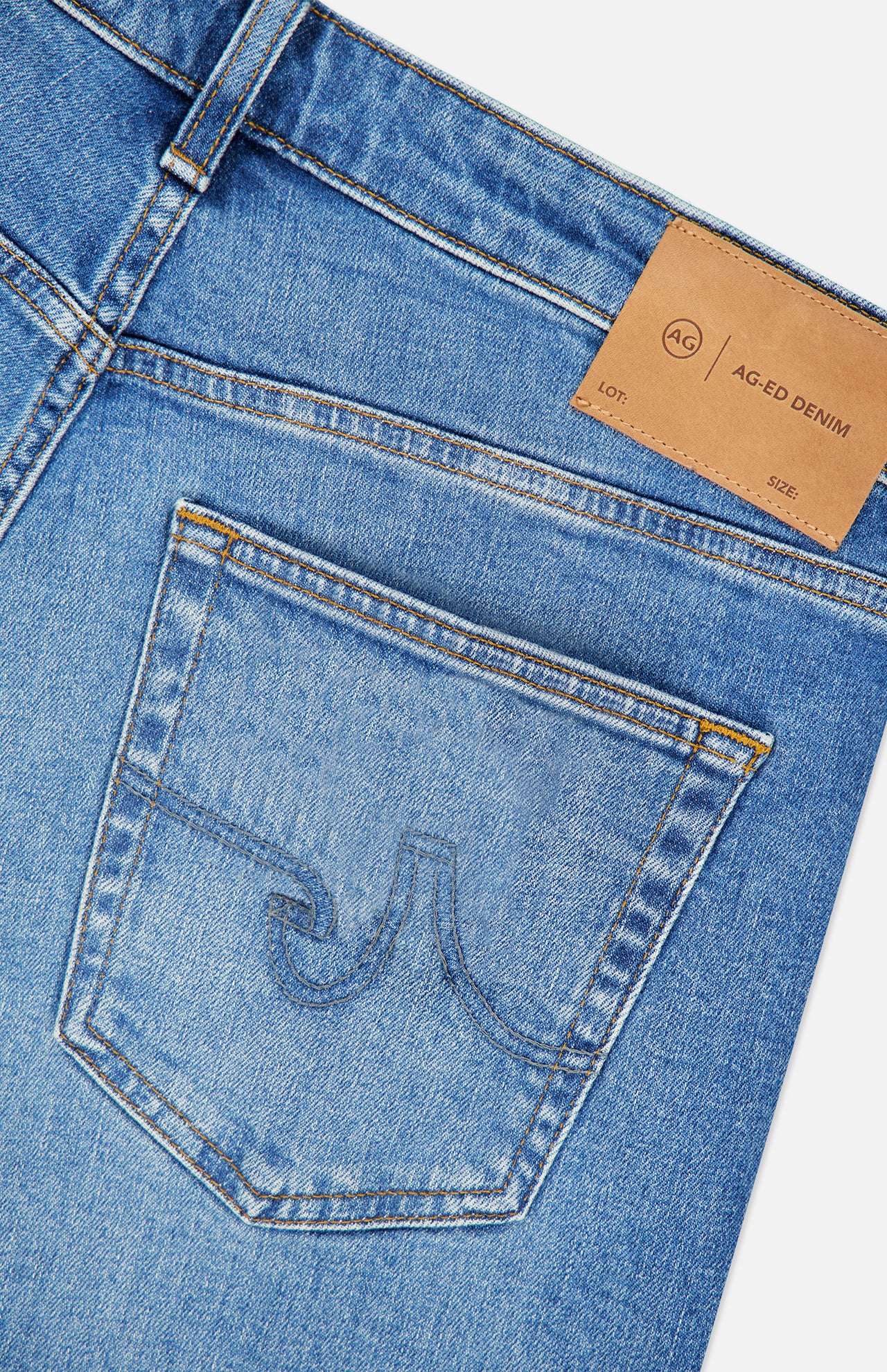 Close-up of blue denim jeans showing a back pocket with vintage detail stitching and a brown leather patch labeled AG near the waistband. The Protege Jean in 14 Years by AG features a straight leg fit, highlighting classic craftsmanship and timeless appeal.