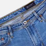 Close-up of the waistband and upper section of AG's Protege Straight Leg Jeans in Promise, showing the button, zipper, belt loops, and front pockets against a white background.