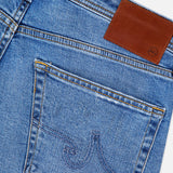 Close-up of the back pocket and waistband of AG Protege Straight Leg Jeans in Promise, featuring golden stitching, a brown leather patch, subtle pocket detailing, and crafted with stretch for all-day comfort.