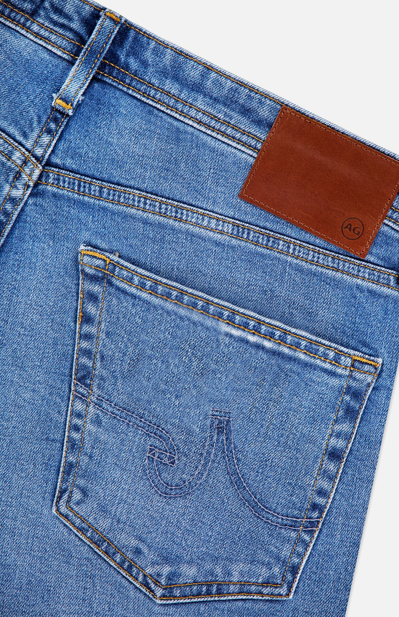 Close-up of the back pocket and waistband of AG Protege Straight Leg Jeans in Promise, featuring golden stitching, a brown leather patch, subtle pocket detailing, and crafted with stretch for all-day comfort.