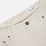 Close-up of the waistband and upper front of AG Protege Pants in Pumice, highlighting the button, zipper, belt loops, and interior tags with a label reading PROTÉGÉ Classic Straight Italian Fabric.