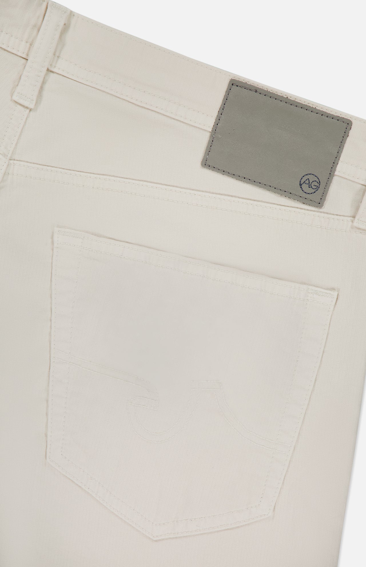 Close-up of the back pocket and waistband of AG's Protege Pants in Pumice denim, featuring a light gray leather patch with the AG logo above the pocket.