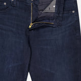 The AG Tellis Slim Jeans in Tamarack are dark blue with a slightly faded texture, classic pockets, and belt loops. Shown with the zipper and top button undone to reveal the inside waistband and fly area.