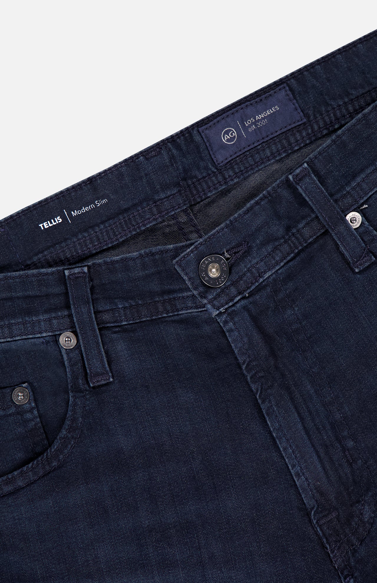 Close-up of the Tellis Slim Jeans in Tamarack by AG, featuring a dark blue wash, slim fit, waistband, front button, zipper, belt loops, and front pockets. Stylish men's jeans with AG Los Angeles label inside.