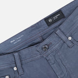 A close-up of the AG Tellis Sueded Sateen Pants in Blue Grain, featuring Italian stretch fabric with a microsueded finish, and details like the waistband, button, front pockets, and the Tellis Modern Slim Italian Fabric label inside.