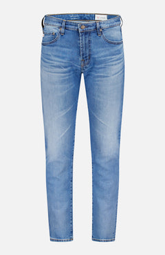 The AG Tellis Aged Jeans are slim-fit, light blue denim with a classic five-pocket design and button closure, shown against a plain white background.