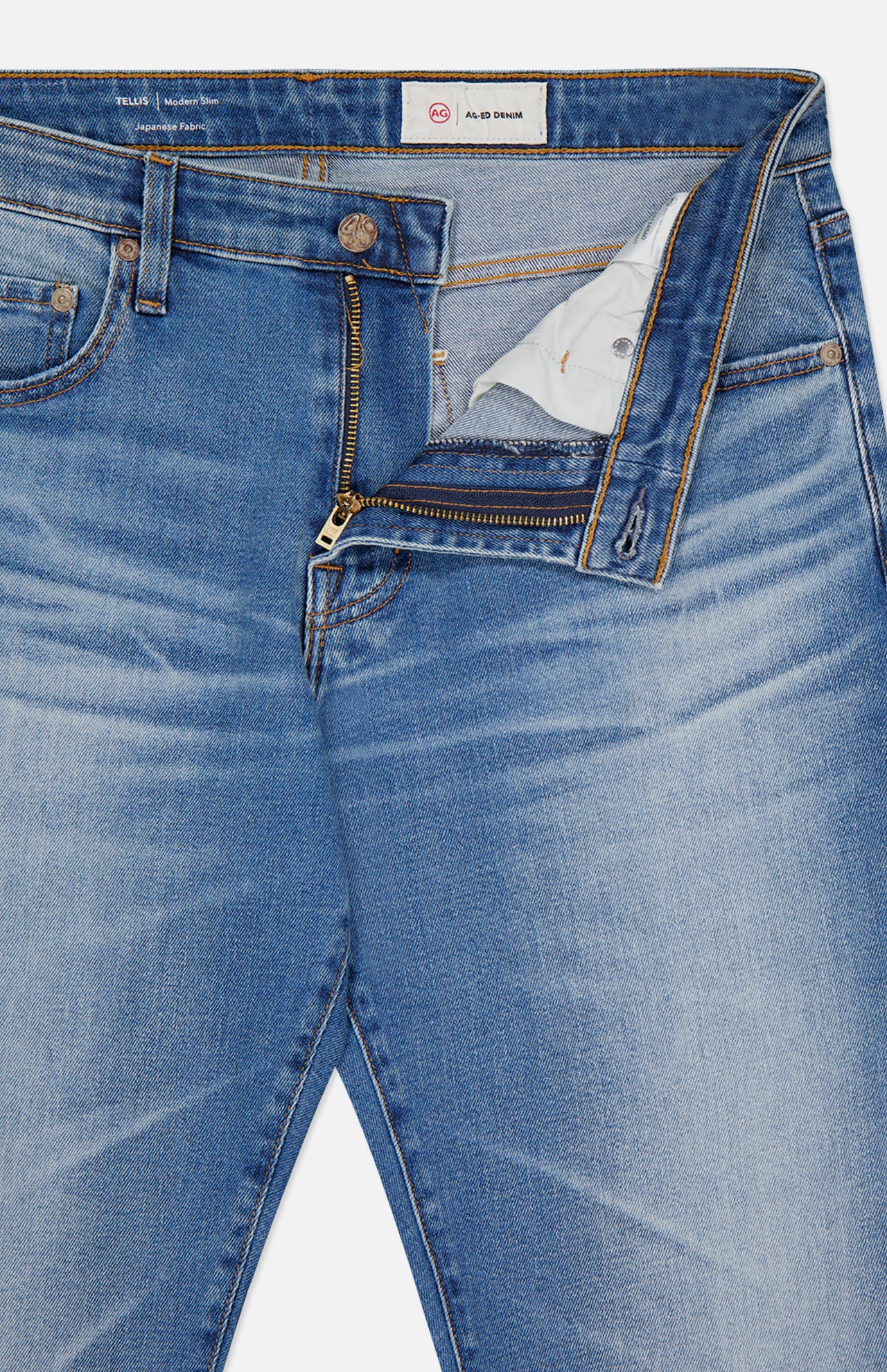 The Tellis Aged Jeans by AG are slim fit, light blue denim with a partially unzipped fly revealing the inner pocket lining and waistband label.