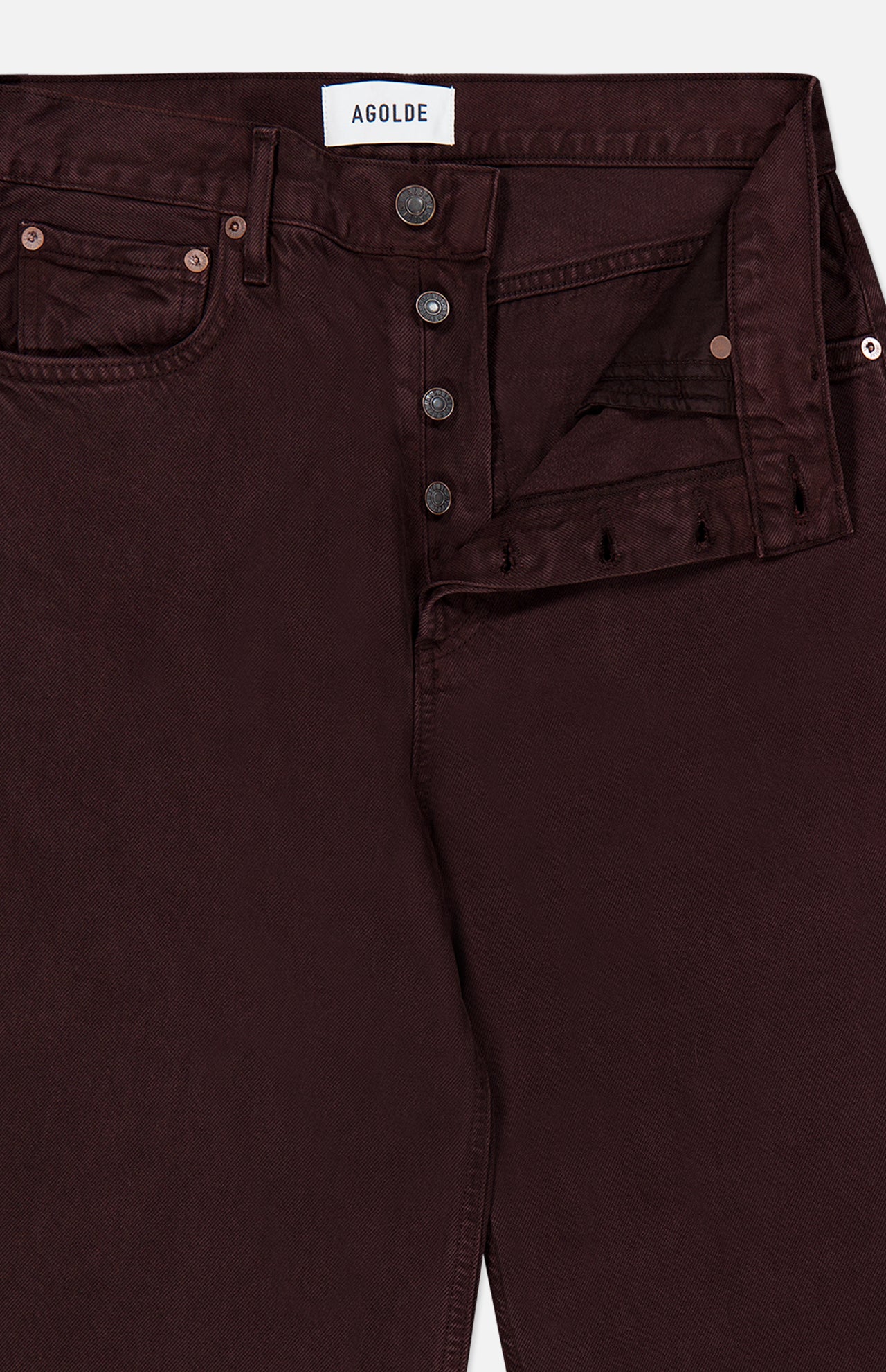 Close-up of the AGOLDE Ren Jean in Sloe Berry, a pair of burgundy high rise, cropped jeans featuring a partially open button fly with four metal buttons, front pockets, and a visible white AGOLDE label inside the waistband—offering a modern take on classic denim.