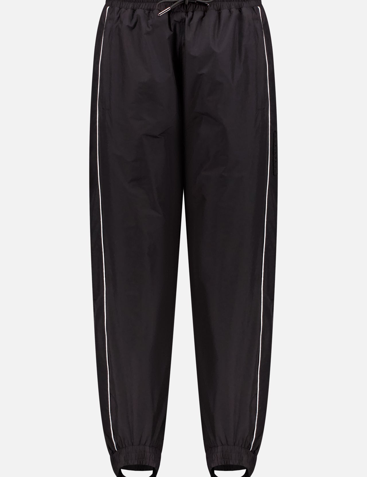 The Fuseau Stirrup Track Pants by ALAINPAUL feature black fabric with white piping, an elastic waistband with drawstring, elastic cuffs, and ankle stirrups for a dance-inspired look. Shown on a plain white background.