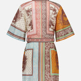 The Alberta Mini Linen Dress by ALEMAIS is a short-sleeved, belted bohemian mini with a patchwork of tropical and geometric prints in brown, orange, green, and blue. Shown from the back against a white background.