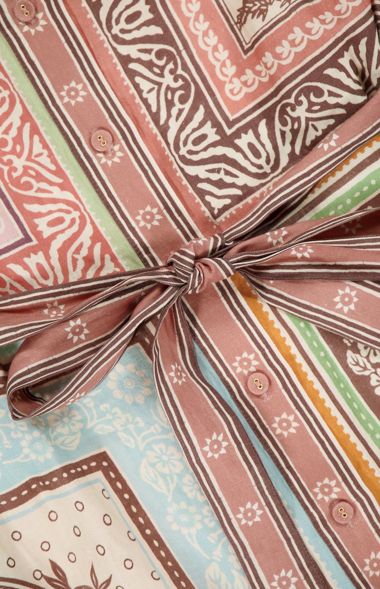 Close-up of the ALEMAIS Alberta Mini Linen Dress, showcasing a brown, pink, green, and blue geometric and floral print with a tied waist bow and small front buttons.