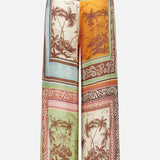 The Alberta Silk Pull-on Pant by ALEMAIS features a wide-leg, relaxed fit and showcases tropical island scenes, palm trees, and ocean views in earthy tones, bordered with patterned frames for a bohemian look.