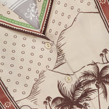 Close-up of the Alberta Silk Relaxed-fit Shirt by ALEMAIS, in patterned beige with brown buttons, featuring palm trees, car, mountains, polka dots, and earthy borders—perfect for resort wear.