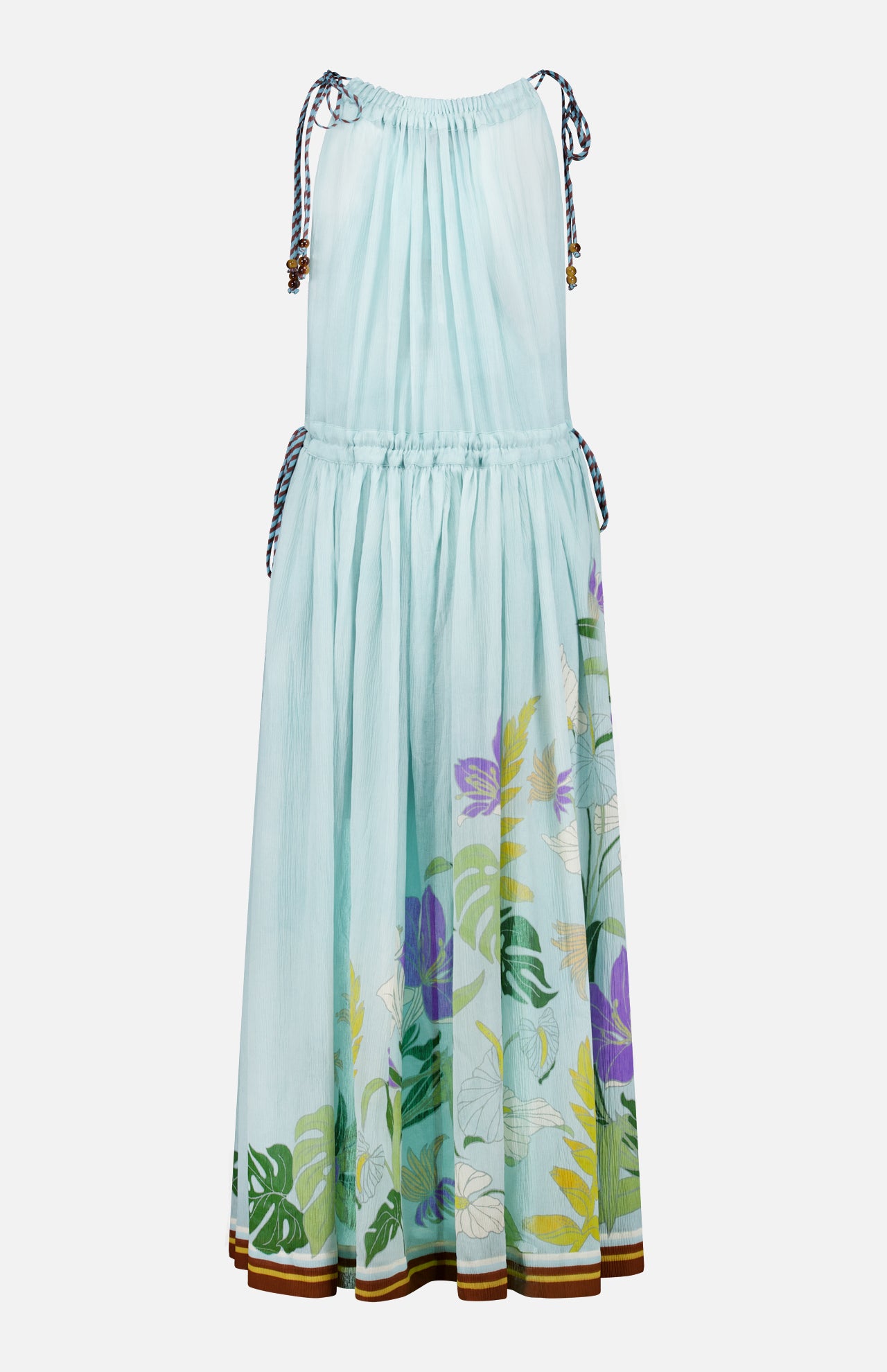 The Alfie Sleeveless Midi Dress by ALEMAIS is a light blue cotton dress with shoulder ties, gathered neckline, flared skirt, floral print featuring colorful leafy accents near the hem, and brown trim along the bottom edge.