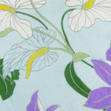 The Alfie Sleeveless Midi Dress by ALEMAIS features a floral print with white and purple flowers with yellow centers, green leaves, and stems on a light blue background.