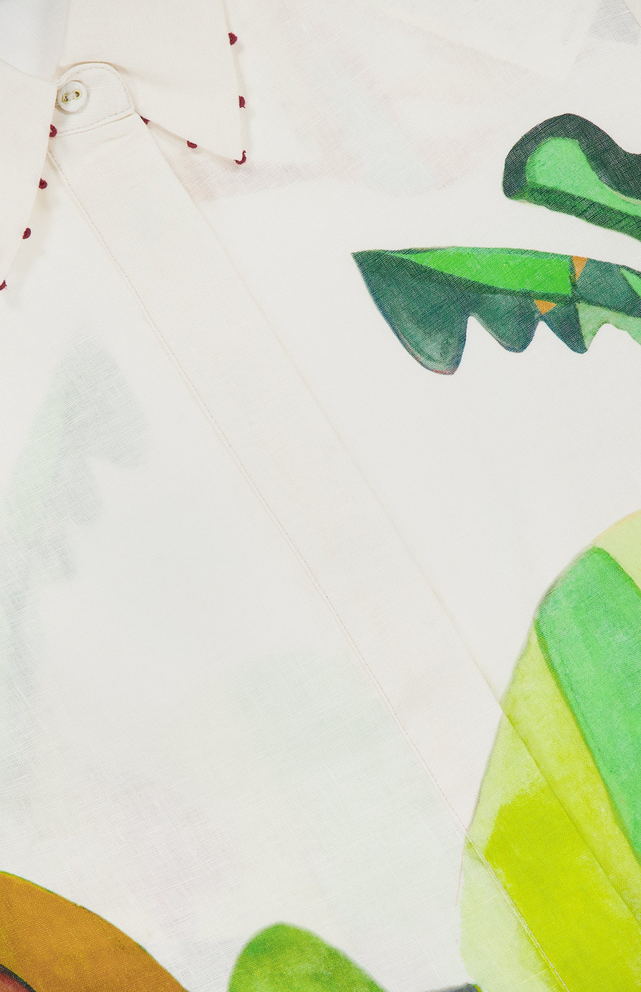Close-up of the ALEMAIS Mokshini Artist Collab Shirt, a white button-down with visible stitching and a vibrant abstract leaf print in green, yellow, and brown.