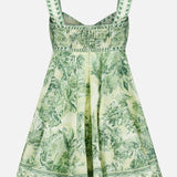 The Sara Mini Twist Sundress by ALEMAIS is a green and white flared mini dress with wide straps, a smocked bodice, and a tropical palm print—perfect for sunny days.