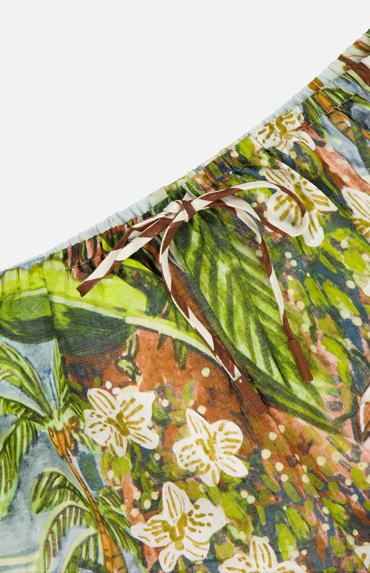 Close-up of the ALEMAIS Toucan Tango Linen Short, showcasing a tropical floral print in green, brown, and white with an elastic waistband and brown drawstring—ideal for effortless vacation style.