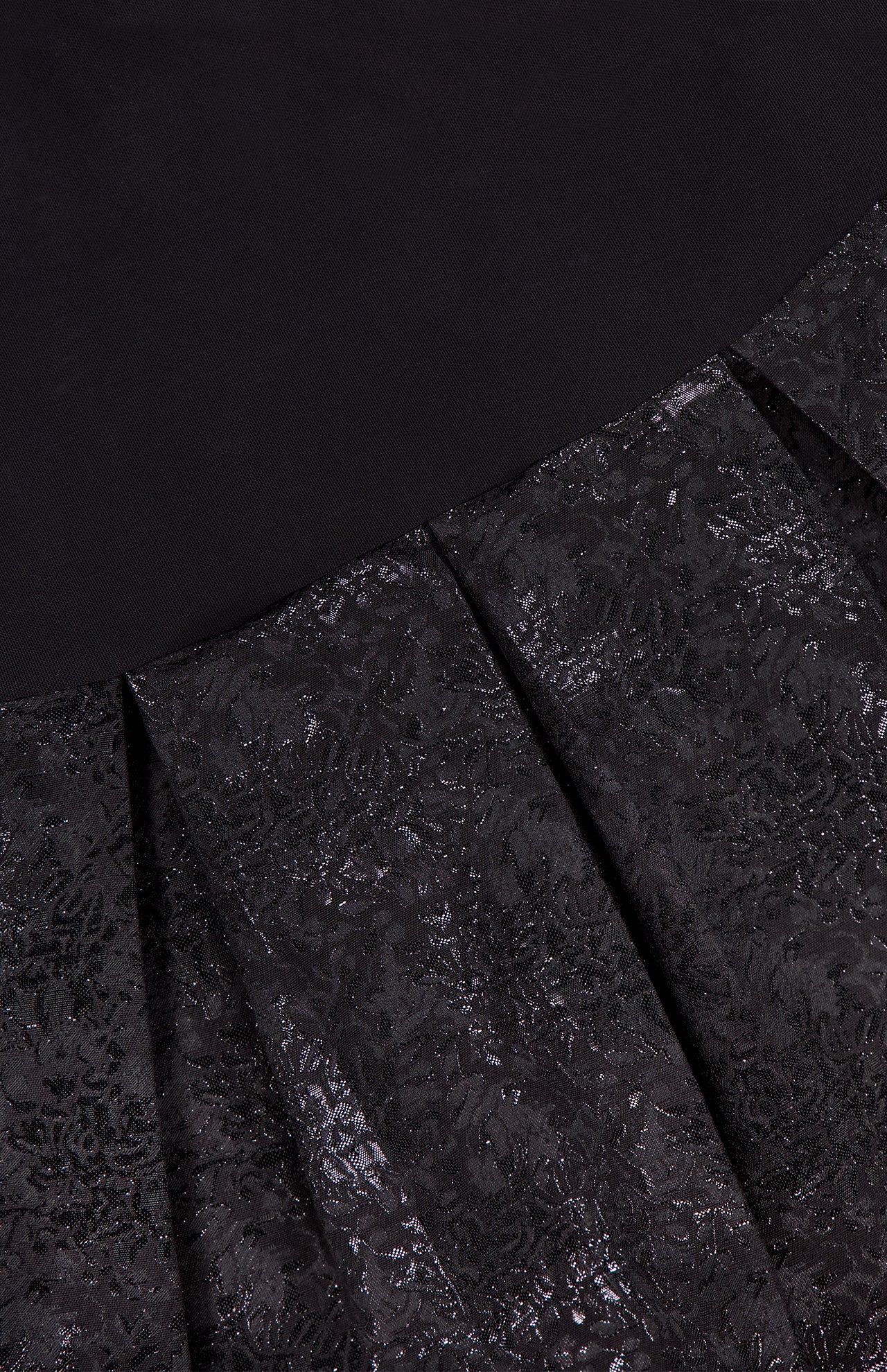 Close-up of the Chara Embellished Neckline Sleeveless Mini Dress by ALICE + OLIVIA, featuring black jacquard fabric with shiny, intricate floral patterns and pleats that transition to a solid black area at the top.