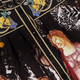 Close-up of the ALICE + OLIVIA Cora Voluminous Long Sleeve Blouse: a black satin top with classical-inspired women’s faces and floral prints in yellow, blue, and green near the collar, blouson sleeves, and black front buttons.