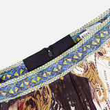 A close-up of the ALICE + OLIVIA Katz Maxi Pleated Skirt With Slit, showcasing its colorful, ornate classical artwork pattern, intricate blue and gold waistband designs, black zipper, and a partially visible white clothing label.