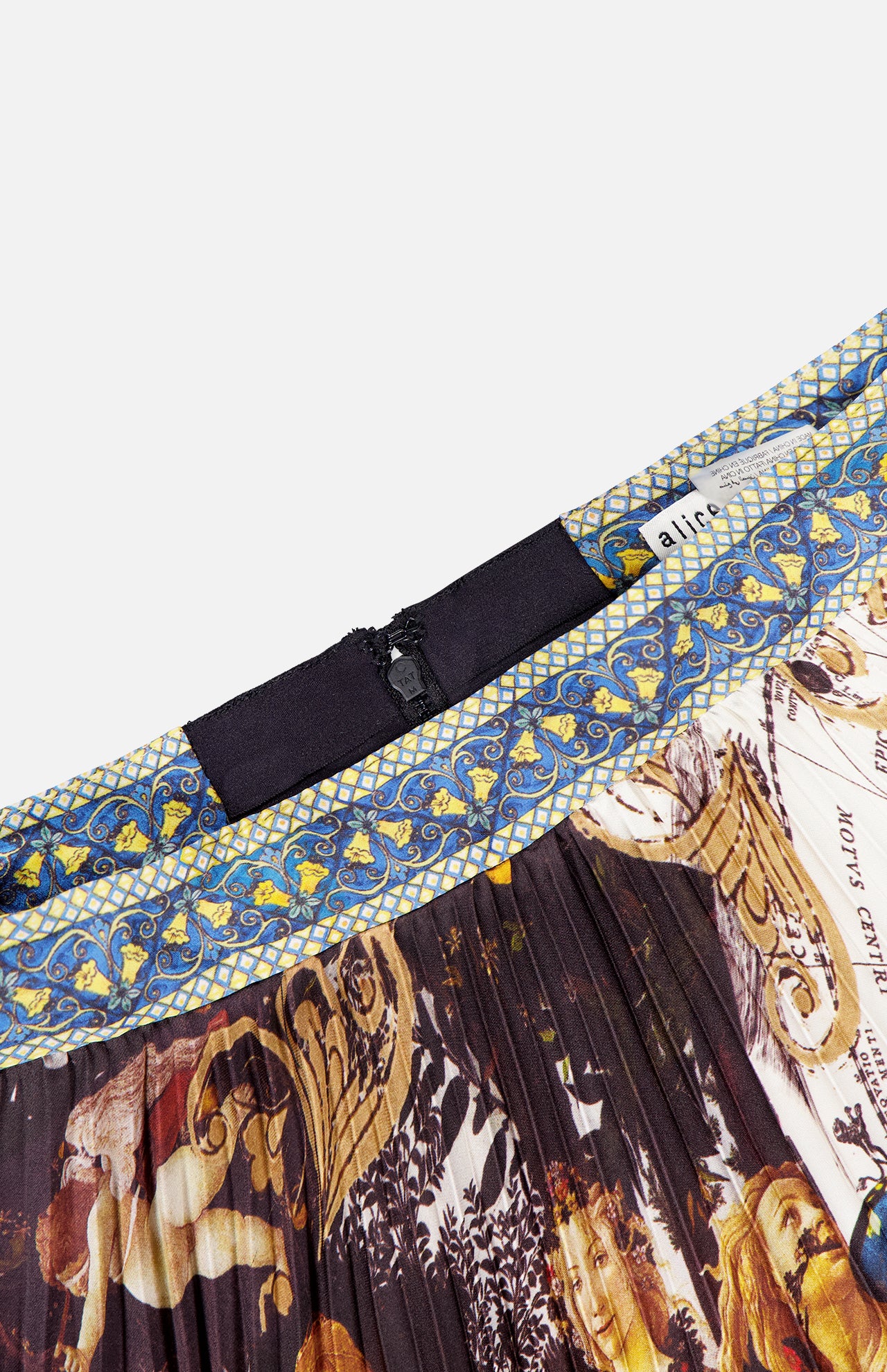 A close-up of the ALICE + OLIVIA Katz Maxi Pleated Skirt With Slit, showcasing its colorful, ornate classical artwork pattern, intricate blue and gold waistband designs, black zipper, and a partially visible white clothing label.