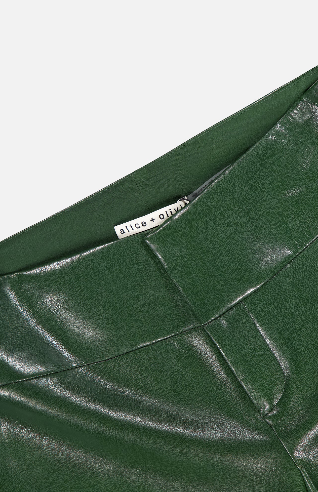 Close-up of the waistband and upper section of the Olivia Vegan Leather Fit Flare Pant in shiny, dark olive by ALICE + OLIVIA, featuring a visible brand label inside.