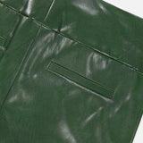 Close-up of the Olivia Vegan Leather Fit Flare Pant by ALICE + OLIVIA, showing its smooth dark green surface, horizontal slit pocket, and visible stitching details.