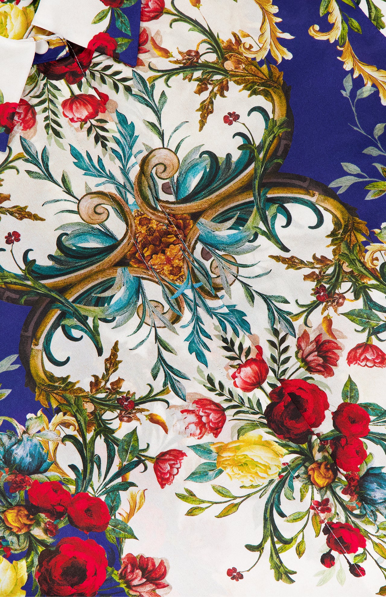 A close-up of the Willa Concealed Placket Top by ALICE + OLIVIA, showcasing vibrant red, yellow, and pink florals with green leaves and gold scrollwork on a white and deep blue crepe de chine fabric.
