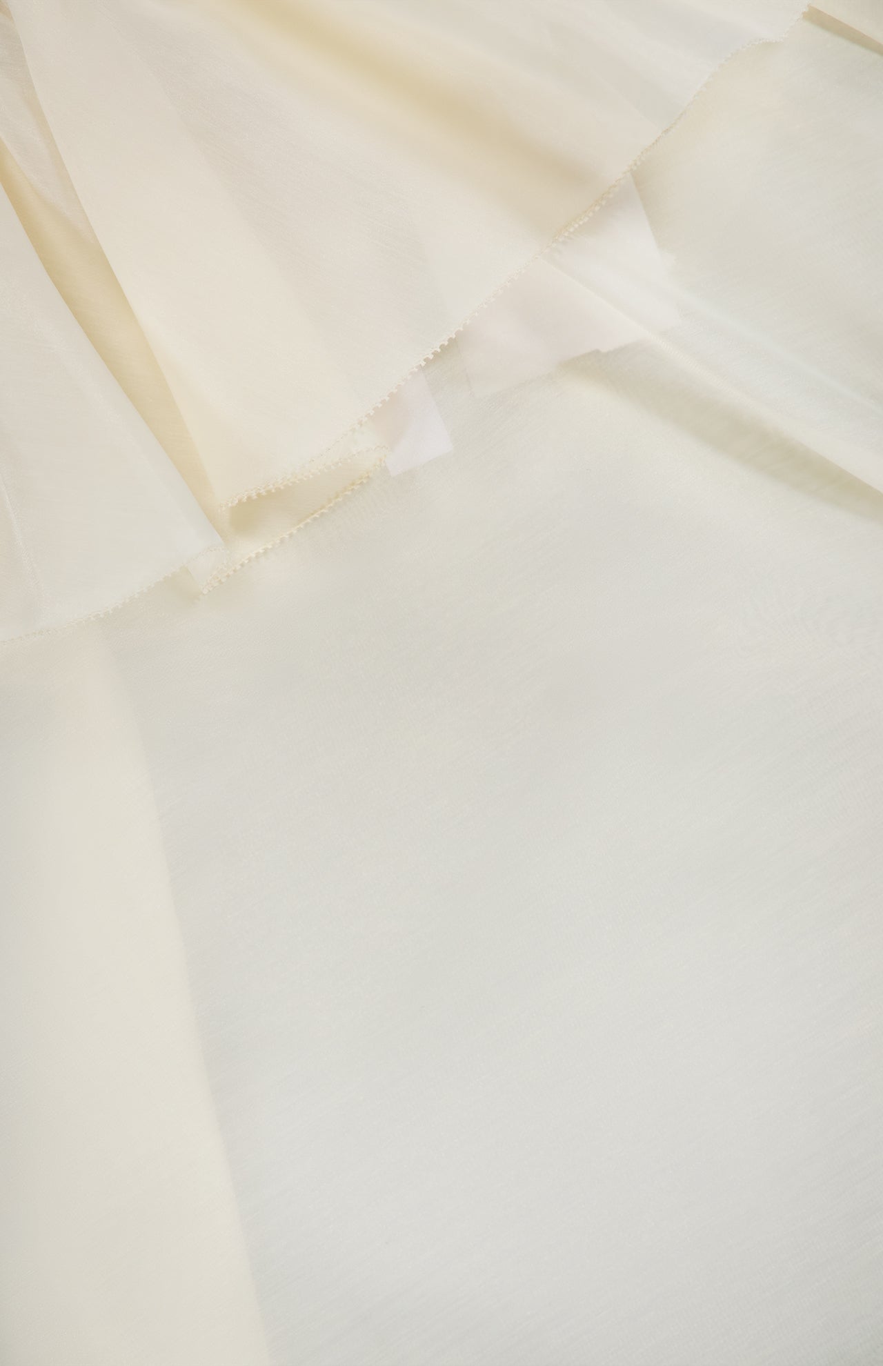 Close-up of layered, sheer organza fabric in off-white or cream with soft folds and a delicate, translucent texture—perfect for the ALICE + OLIVIA Alta Off The Shoulder Ruffle Blouse.