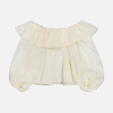 The ALICE + OLIVIA Alta Off The Shoulder Ruffle Blouse features an off-white, sheer organza design with short puffy sleeves and ruffle detailing along the neckline. It is displayed against a plain white background.