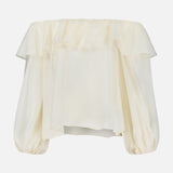 ALICE + OLIVIA’s Alta Off The Shoulder Ruffle Blouse features a cream hue, ruffled neckline detail, billowy long sleeves made of sheer organza, and a loose, flowy silhouette.