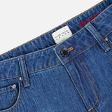 Close-up of the waistband of the Low Rise Baggy Jean with Applique in Freyja by ALICE + OLIVIA, featuring blue dark wash denim, a black button, belt loops, and a white ALICE + OLIVIA JEANS label. Red applique detailing is partly visible on the denim, accentuating the baggy silhouette.