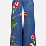 Low-rise baggy jeans in the Freyja wash by ALICE + OLIVIA, featuring a wide-leg dark blue silhouette with bold red and white tulip-shaped embroidered floral appliques on both legs. These jeans are designed with front pockets, a waistband with belt loops, and a button closure.
