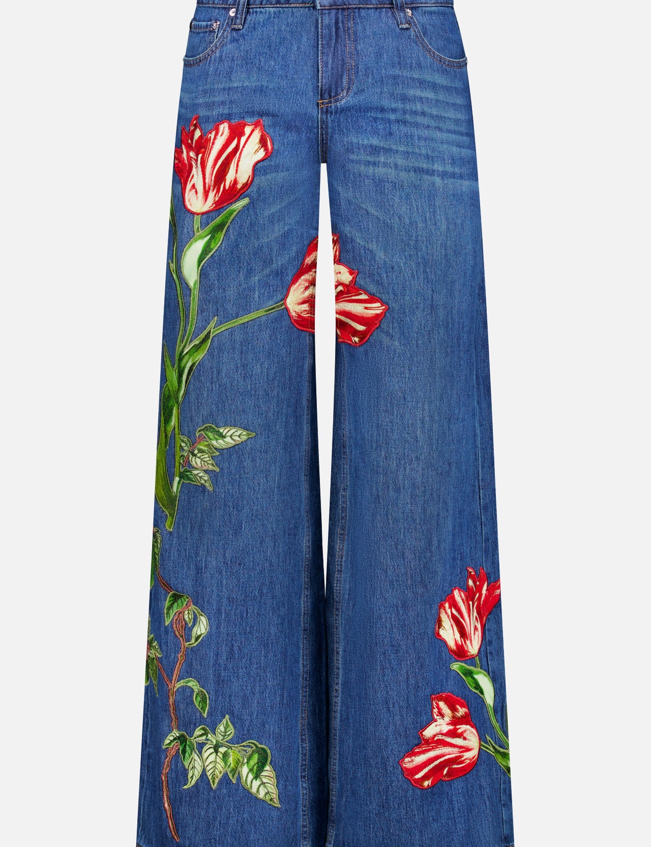 Low-rise baggy jeans in the Freyja wash by ALICE + OLIVIA, featuring a wide-leg dark blue silhouette with bold red and white tulip-shaped embroidered floral appliques on both legs. These jeans are designed with front pockets, a waistband with belt loops, and a button closure.
