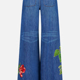 Discover the ALICE + OLIVIA Low Rise Baggy Jean with Applique in Freyja—a wide-leg, dark wash jean featuring back pockets and vibrant embroidered floral and green leaf appliques near the hems of both legs. The relaxed, baggy silhouette is finished with faded detailing at the back of the knees.