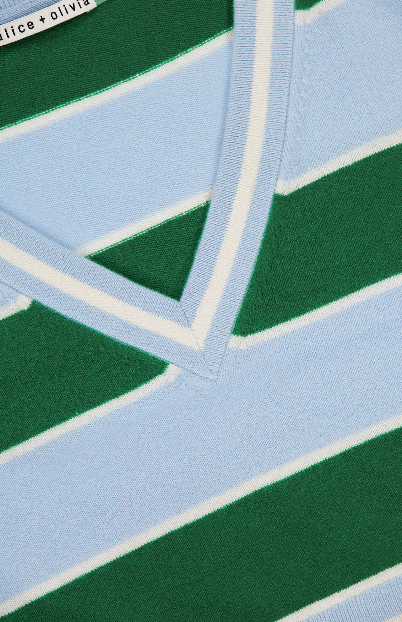 Close-up of ALICE + OLIVIA’s Ayden Cropped V-Neck Pullover Sweater, shown in green, light blue, and white stripes with a double white stripe border at the neckline. A partial brand label is visible—ideal for layering.