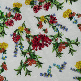 The Cindy Embroidered Cropped T-shirt by ALICE + OLIVIA features white fabric decorated with a vibrant floral design, showcasing red, yellow, orange, and blue flowers with green leaves and scattered sequin embellishments. This cropped t-shirt adds a playful touch to any outfit.